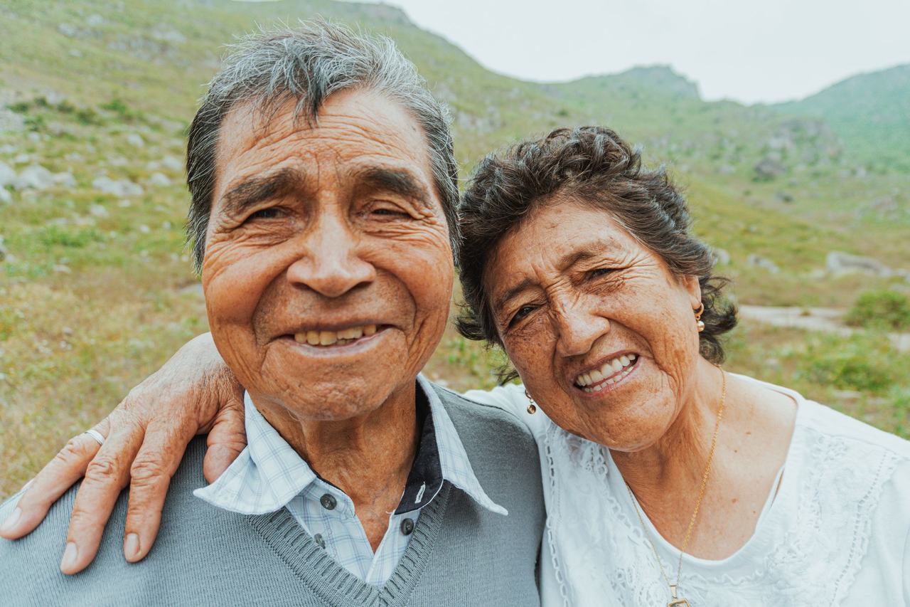 Pareja de adultos mayores sonriendo con montañas al fondo